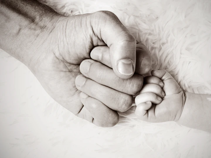 Hand eines Erwachsenen hält die kleine Faust eines Babys